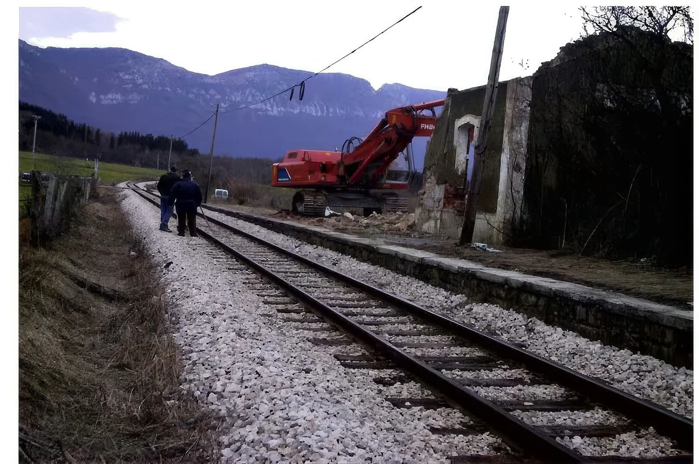 Retroexcavadora derribando una construcción junto a la vía del tren